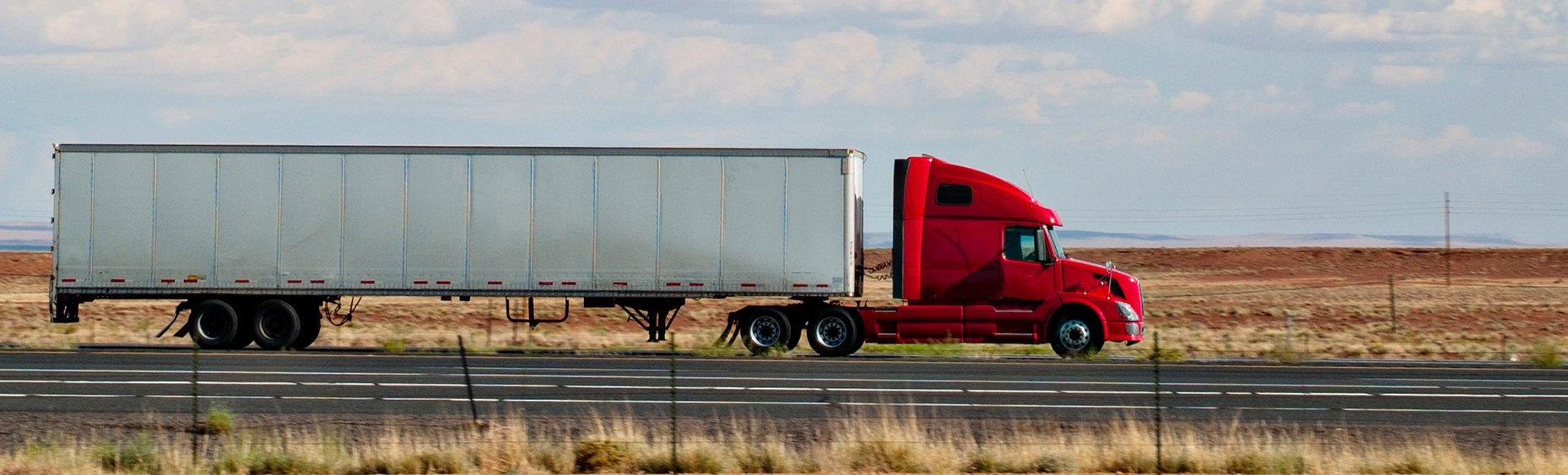 Red tractor-trailer side profile on the highway